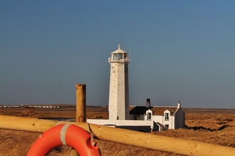 A white lighthouse with grass and a life ring in the foreground 