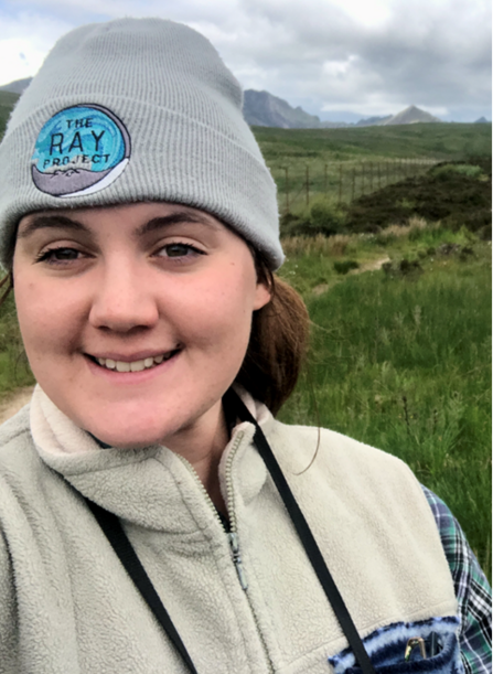 Selfie of Ellena, smiling and wrapped up in a hat and fleece as she is out on a birdwatching walk.